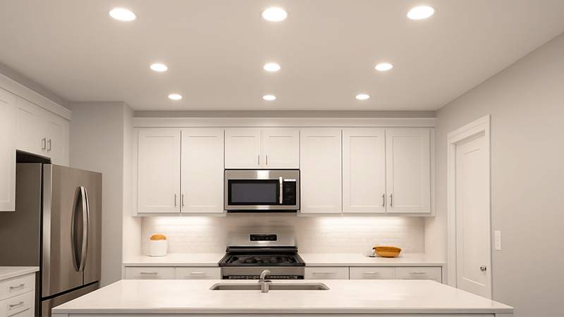A bright, modern kitchen evenly illuminated by several recessed downlights in the ceiling.