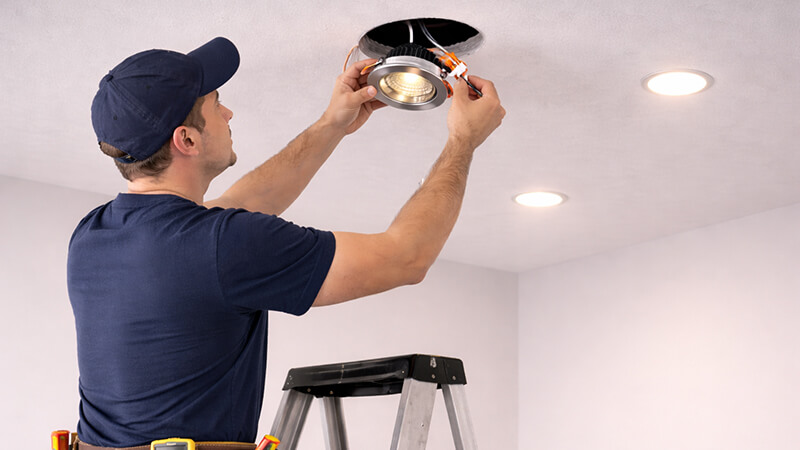 An electrician safely replacing an integrated LED downlight in a modern ceiling.