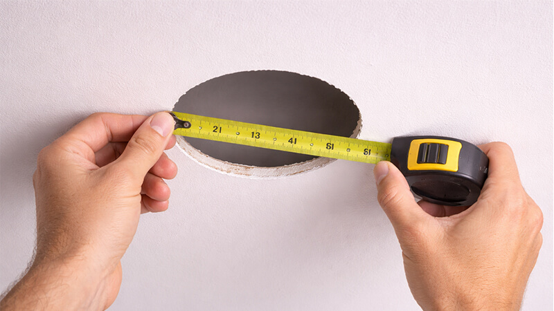 How to Measure a Downlight Cutout person measuring a ceiling cutout hole for a downlight